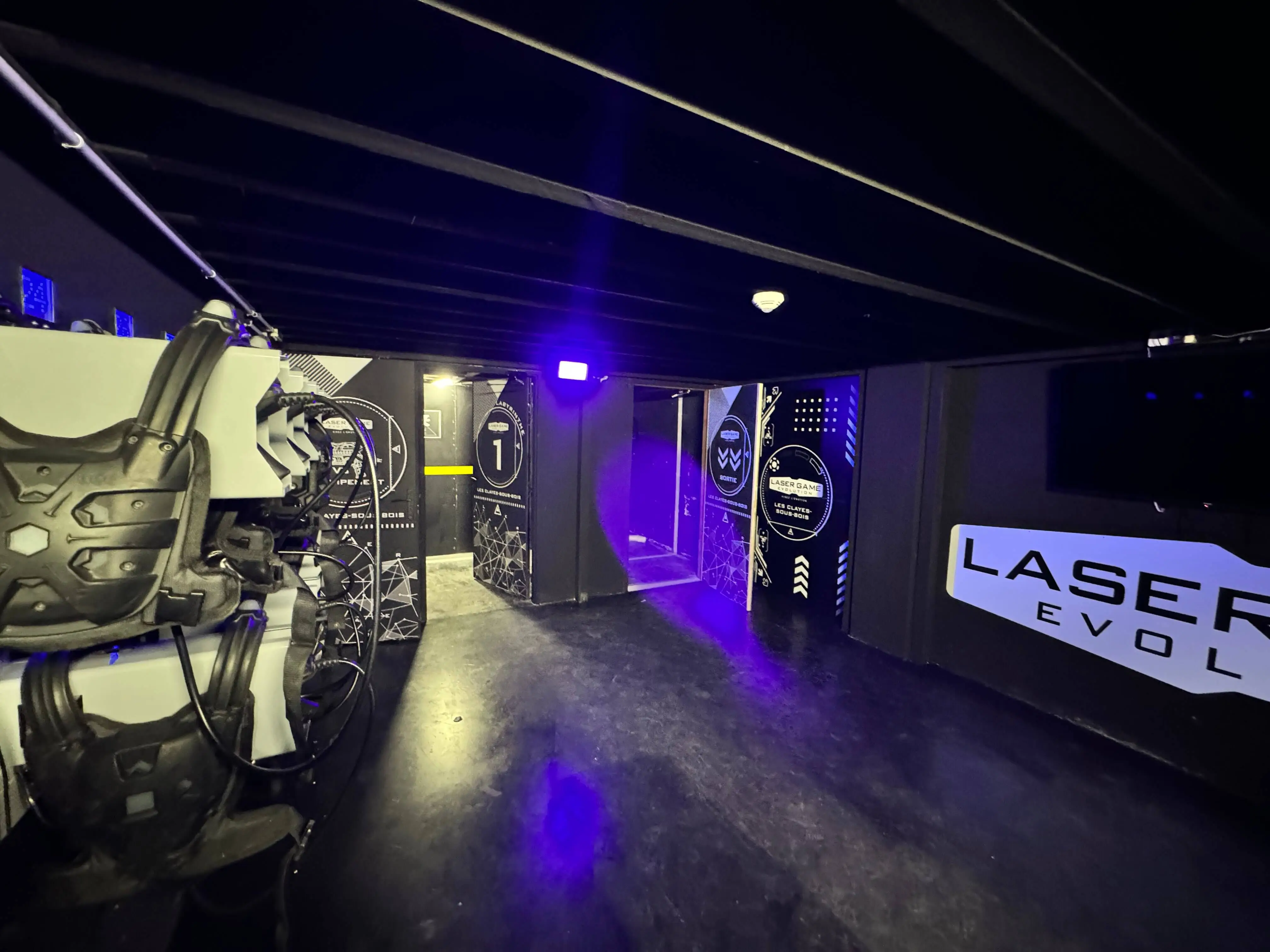 Équipements de Laser Game chez OumCityGames, incluant gilets et pistolets laser sur fond noir éclairé